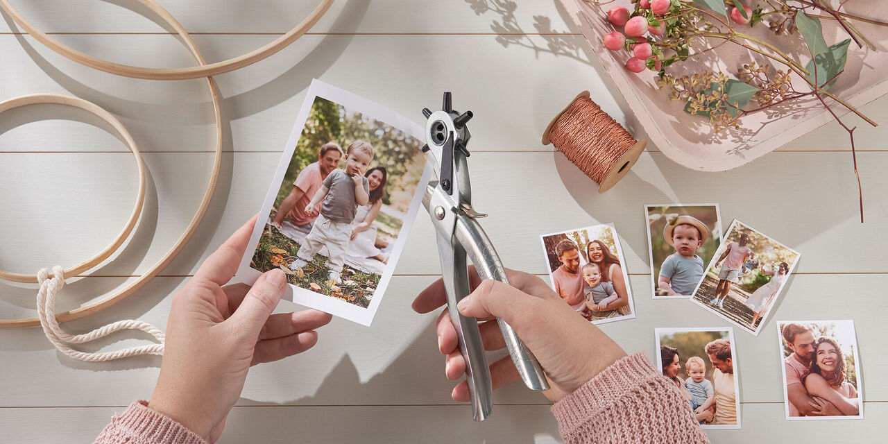 Obrázek dvou rukou, které děrovacími kleštěmi děrují vystřiženou okamžitou fotografii. V pozadí jsou dřevěné kruhy, květiny a ozdobné nitě.